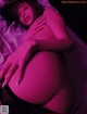 A pregnant woman laying on a bed in a pink light.