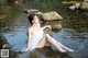 A woman in a white dress sitting on a rock in the water.