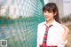 A woman in a school uniform leaning against a fence.