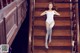 A woman in a white bodysuit is sitting on the stairs.